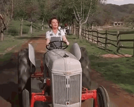gif de uma mulher cantando e dirigindo um trator por uma fazenda