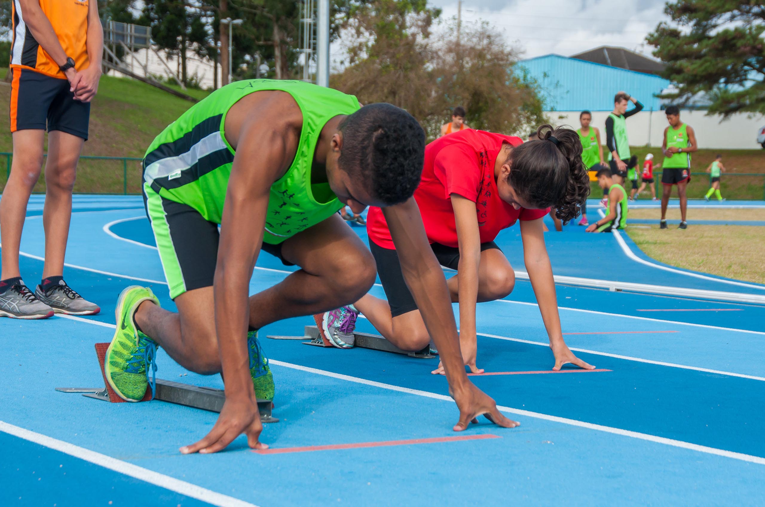 Um estudante e uma estudante na pista de atletismo preparados para iniciar corrida