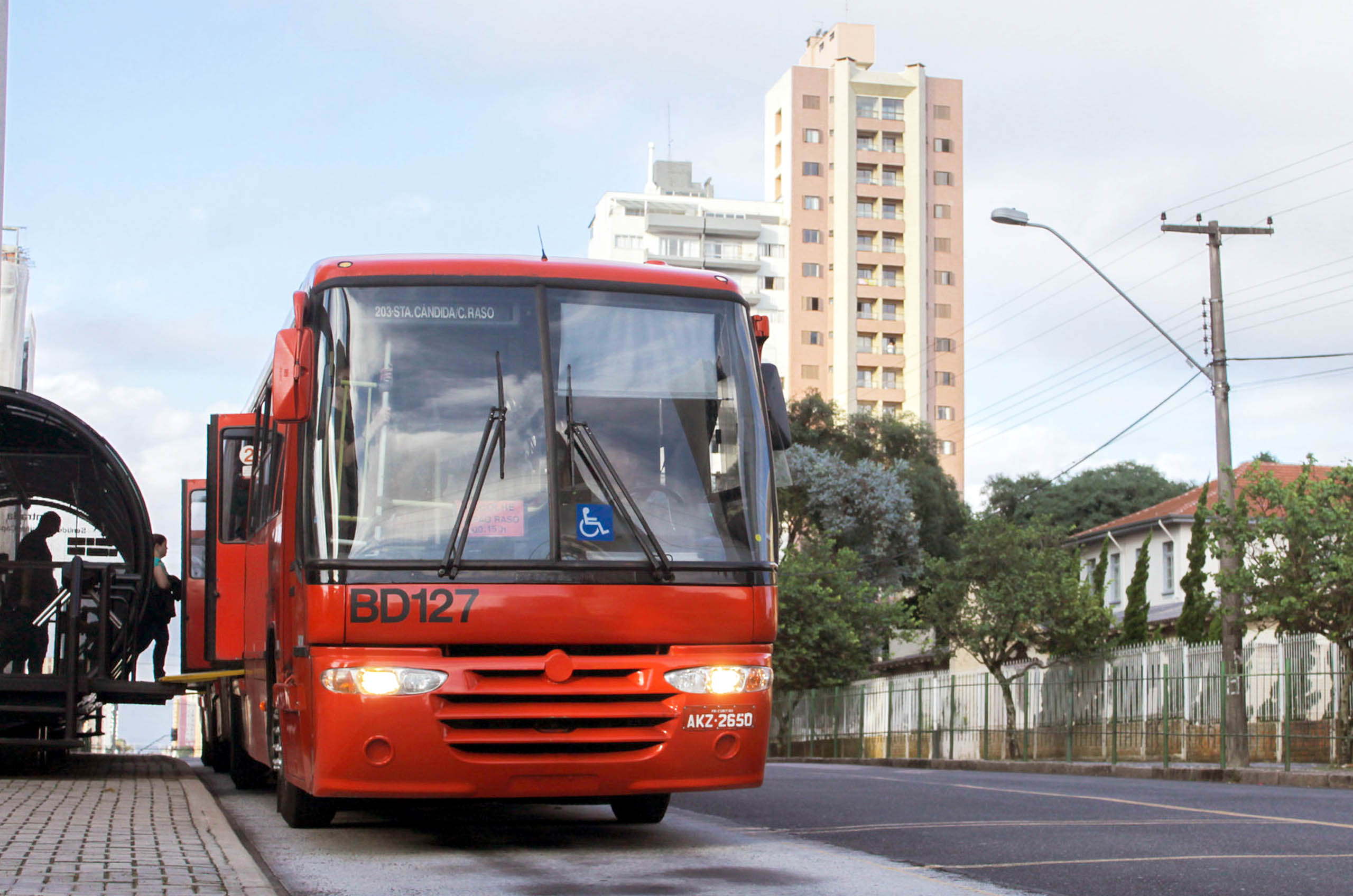 ônibus biarticulado vermelho parado em uma estação tubo, na canaleta exclusiva para esse ônibus