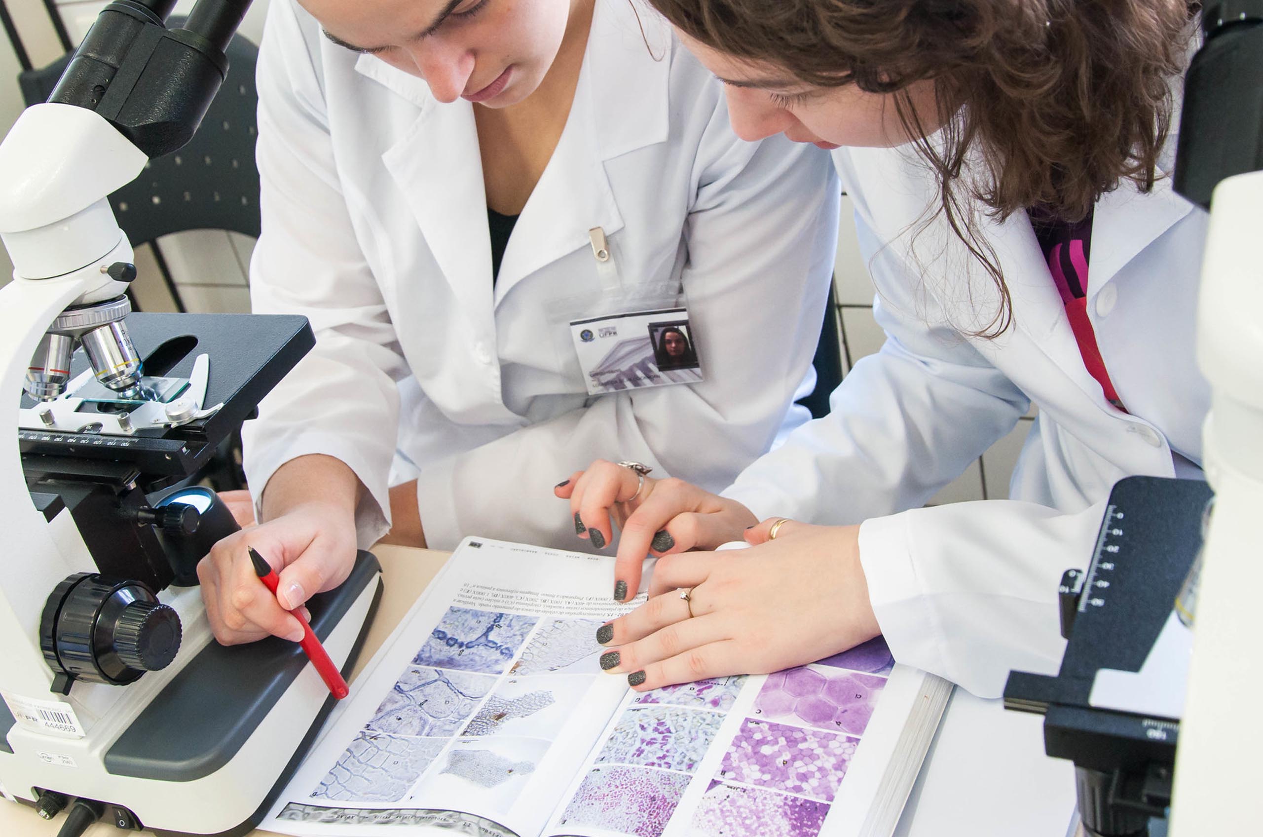 Estudantes consultando livro ao lado de um microscópio