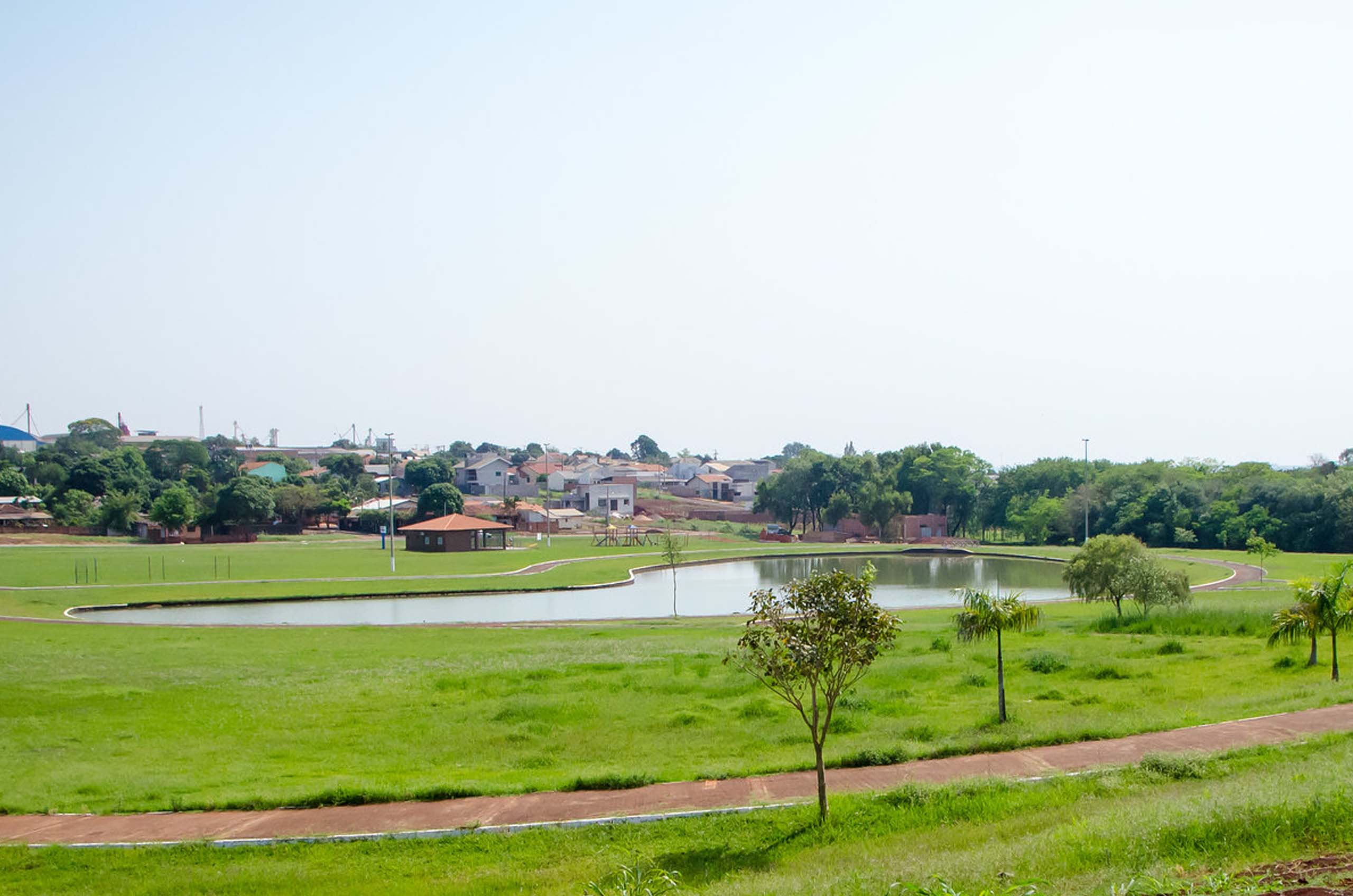 Vista de uma gramado com lago ao centro e casas ao fundo, na cidade de Palotina, Paraná