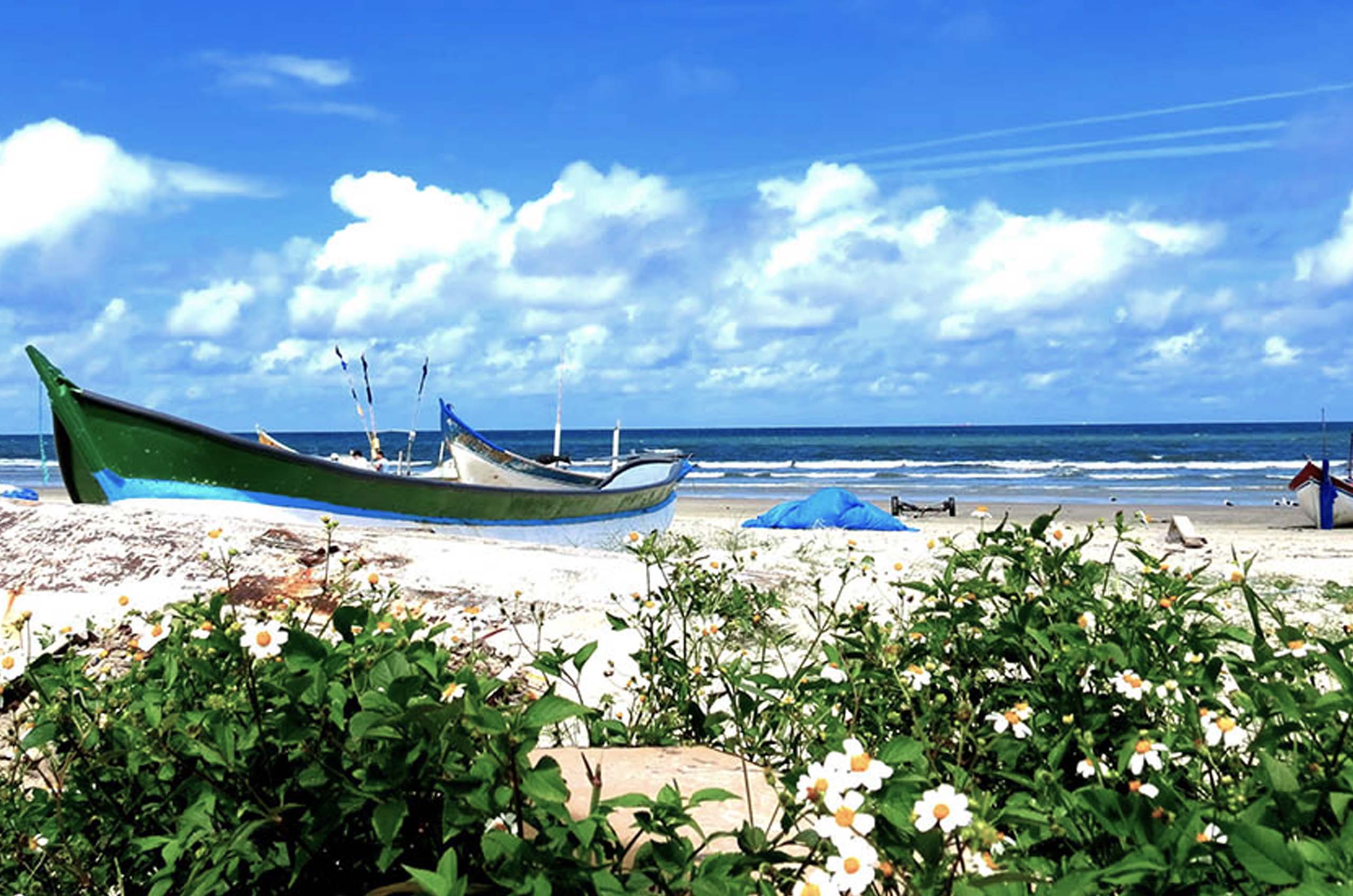 Foto da praia, barco à esquerda na areia e o mar ao fundo.