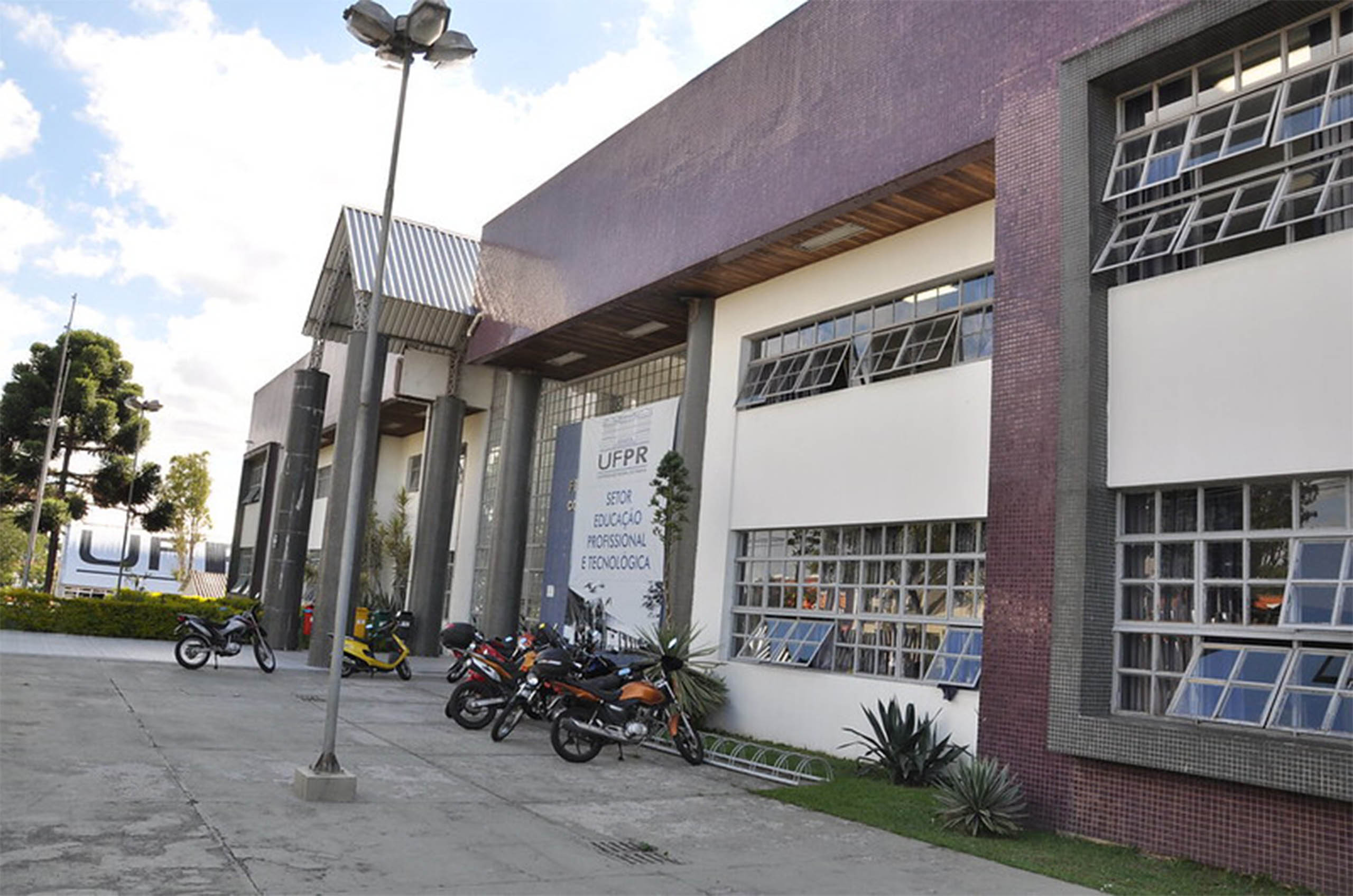 Frente de prédio com muitas janelas, na cor branca e vermelha com motos estacionadas em frente.