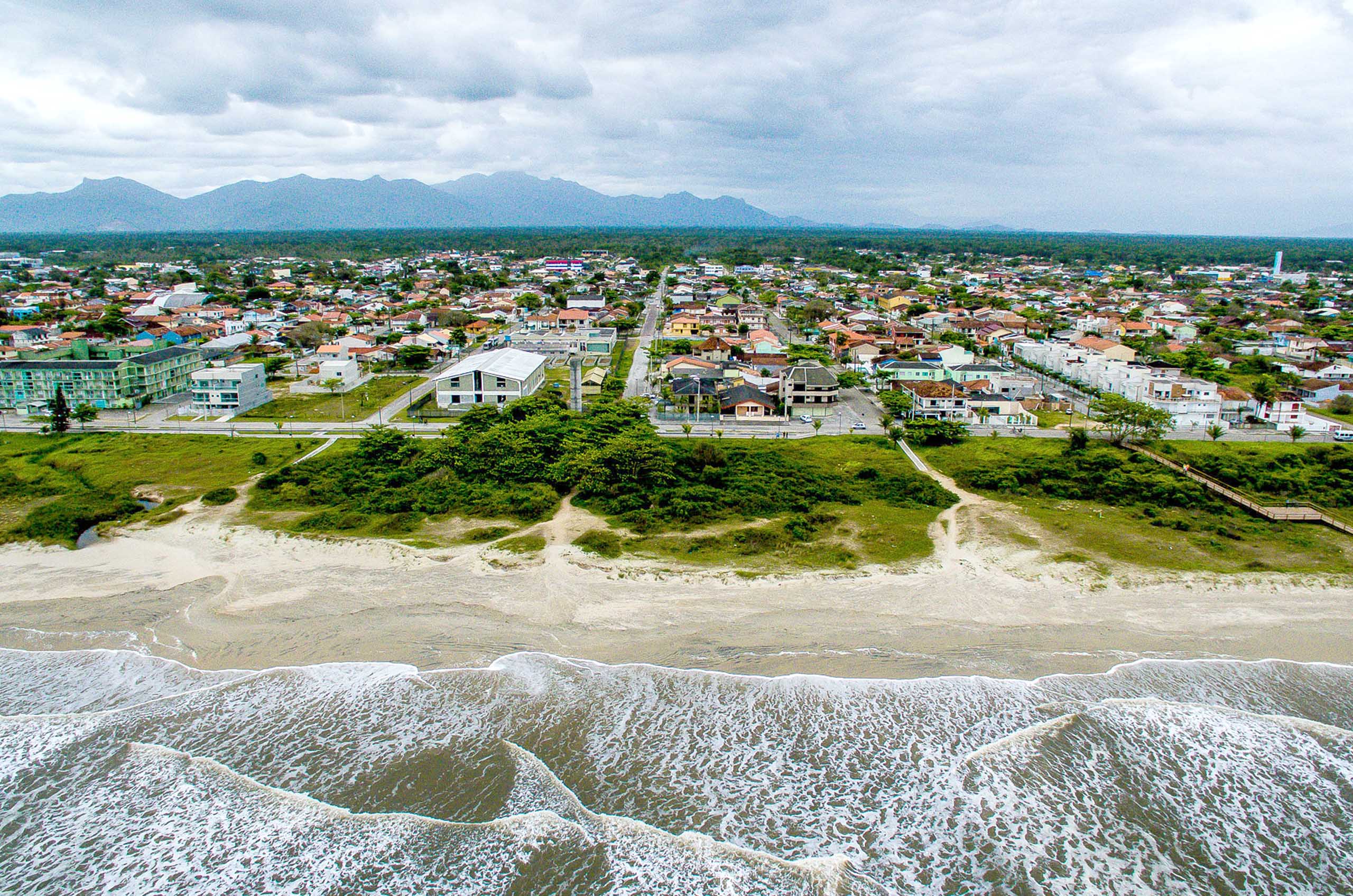 Imagem aérea de Pontal do Paraná; na metade inferior se vê as ondas quebrando na praia, uma pequena faixa de areia e restinga; na metade superior vê-se a zona urbanizada de Pontal do Paraná.